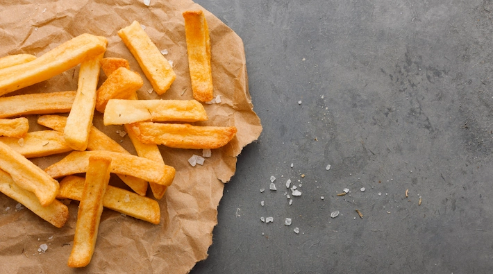 Top view of french fries on paper with salt and copy space